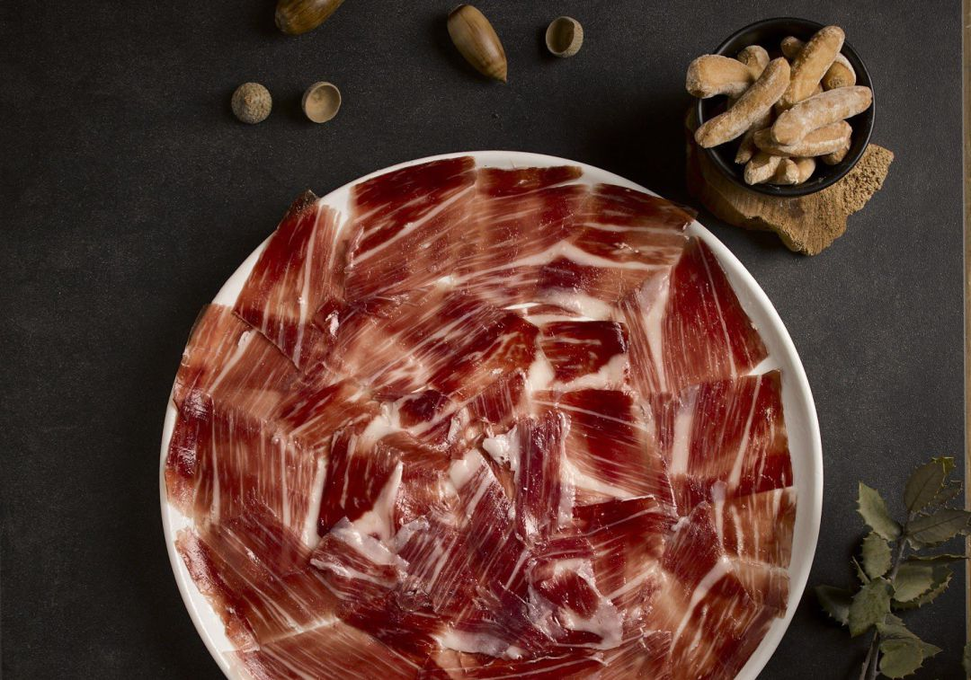 Sugerencia de presentación: plato de ibérico con veteado sobre fondo oscuro, con picos y bellotas.