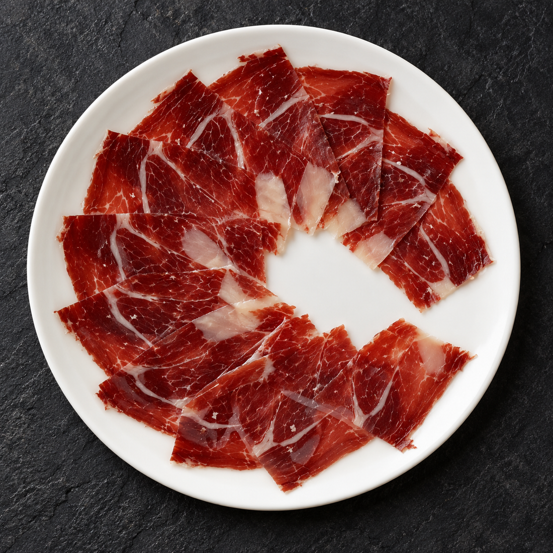 Illustrativt serveringsforslag til Altanza Bellota 100% Ibérico skinke på tallerken, 80 g, maskinskåret med knivskåret effekt.